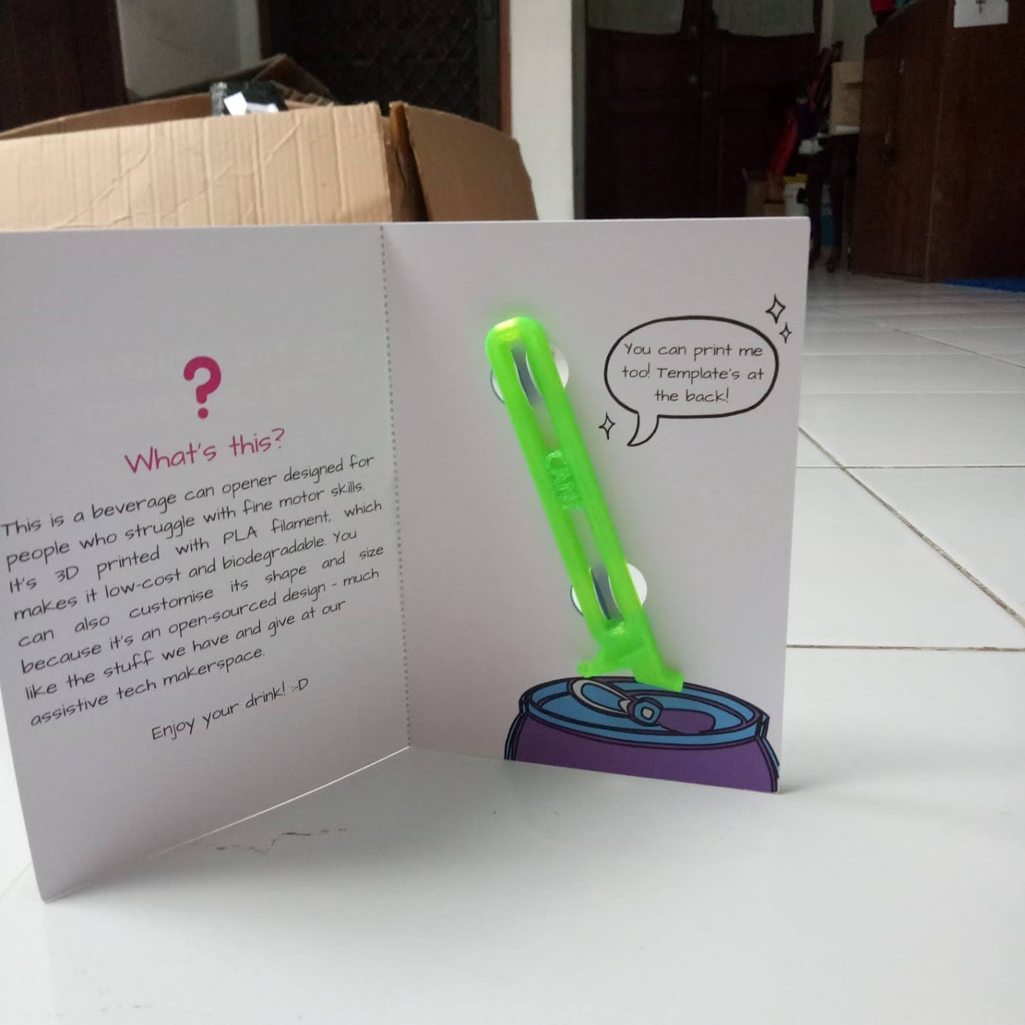 an opened card faced upright with a 3D-printed assistive can opener attached to the second face of the card.